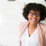 Smiling businesswoman with glasses and afro hairstyle in an office setting.