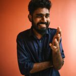 Portrait of a smiling man in a dark blue shirt against a warm terracotta background, conveying happiness.