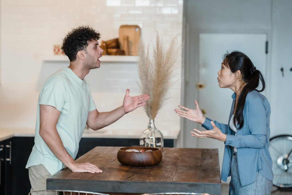 A couple engages in a heated argument at a wooden table in a modern indoor setting.