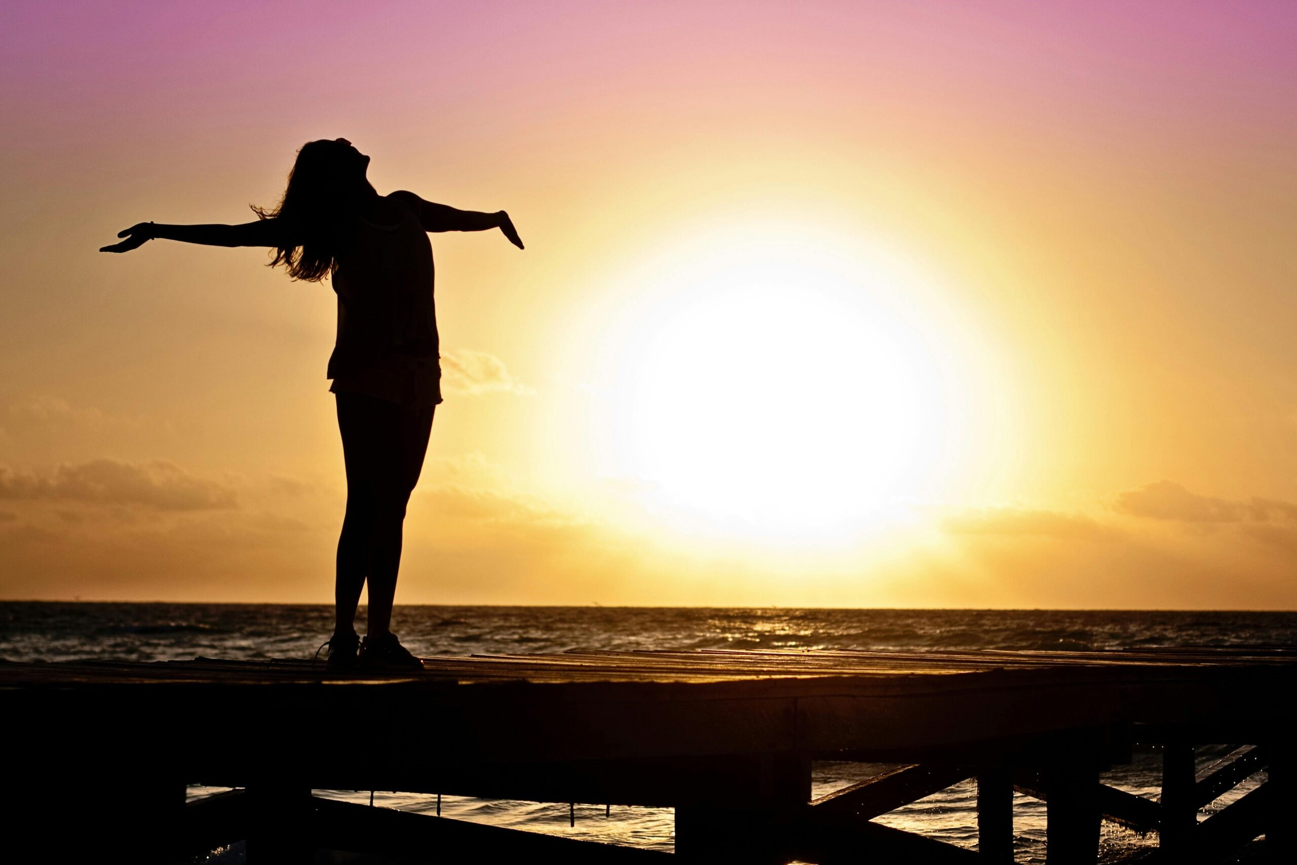 A joyful silhouette of a woman standing on a dock at sunset, embracing the freedom of nature.