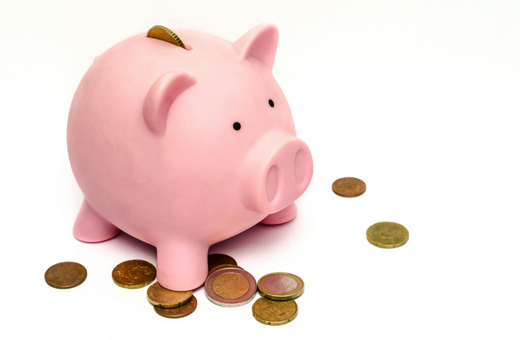 A pink piggy bank surrounded by scattered coins, symbolizing savings and financial investment.