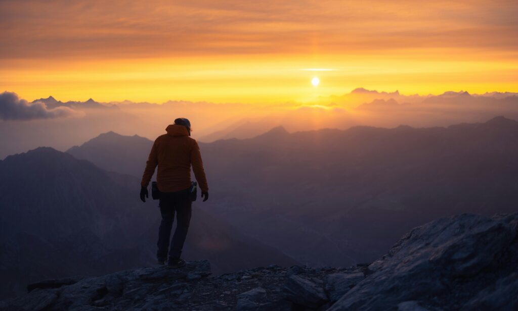 A lone hiker silhouetted against a vibrant mountain sunrise.