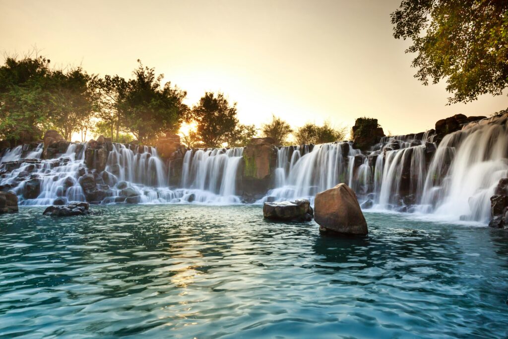 A serene waterfall surrounded by rocks and trees at sunset, radiating tranquility.