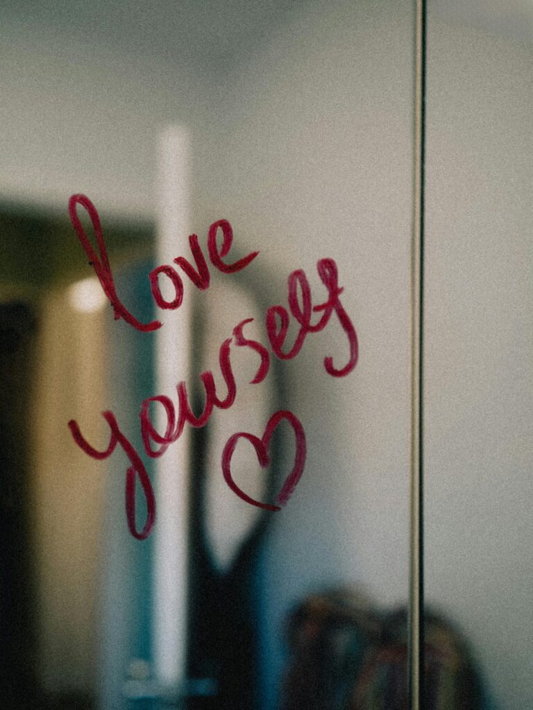 Positive affirmation written on a mirror in red lipstick: Love Yourself.