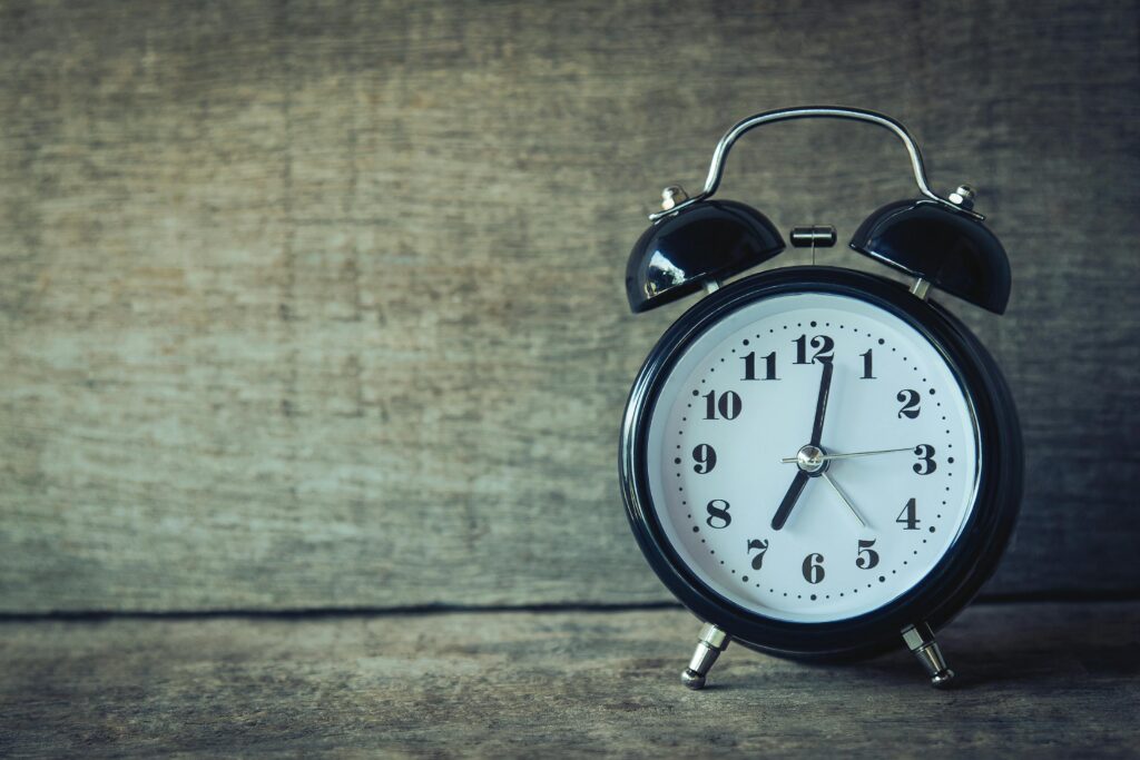 Classic black analog alarm clock on rustic wooden background, perfect for time and nostalgia themes.