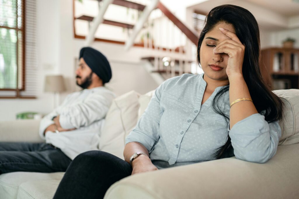 A young couple sitting on a couch indoors, showing signs of stress and frustration.