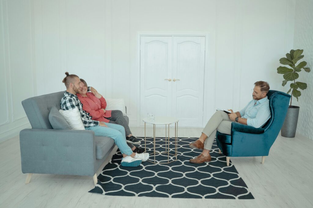 A married couple sits with a counselor discussing relationship issues in a modern office setting.