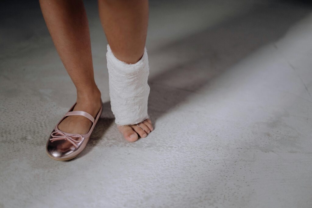 Close-up of a child's leg with an orthopedic cast and a pink shoe on concrete floor.