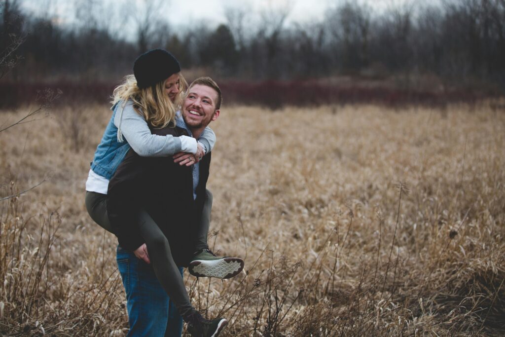 A happy couple enjoys a playful moment in a field during the day, symbolizing love and joy.