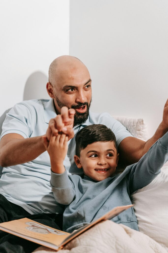 A joyful father and son share a moment reading together in a cozy setting, both smiling and connecting.