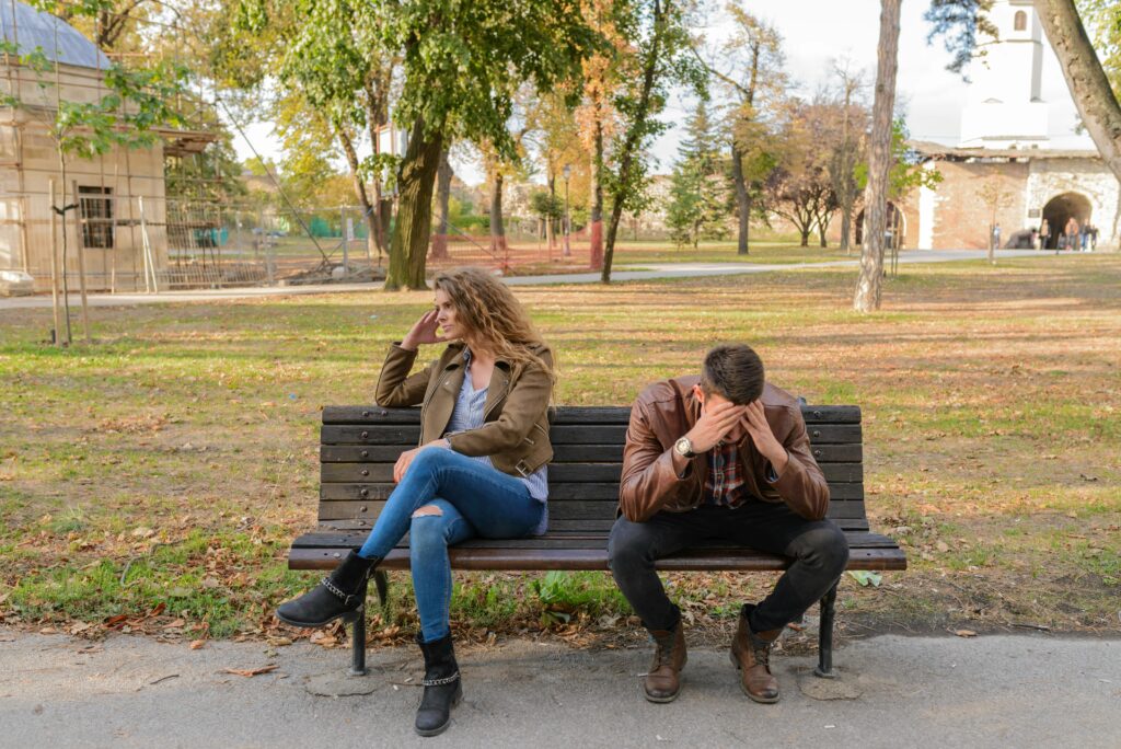 An upset couple seated on a park bench, expressing frustration during an autumn day.